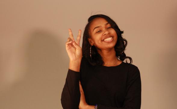 a photo of Heaven in a black top with her hand raised in a peace sign. 