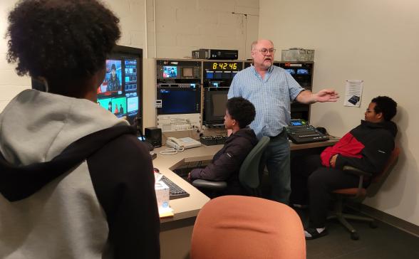 A photography of an instructor teaching three youth how to use the control room for the SPNN studio.