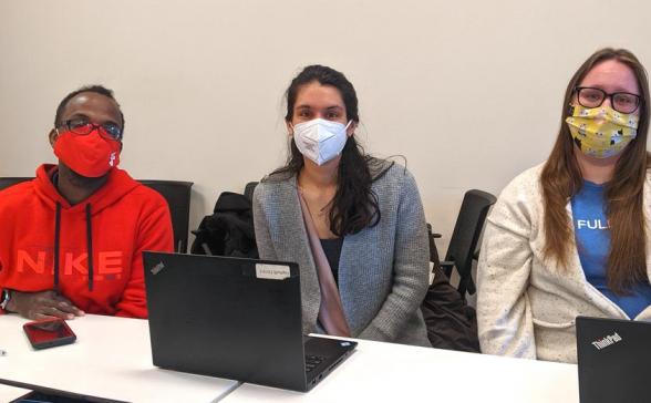 Three members smiling behind laptops and wearing masks