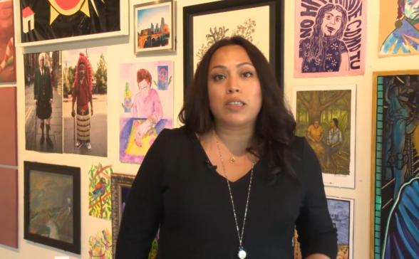 A Latina standing in front of a wall with several different photos. 