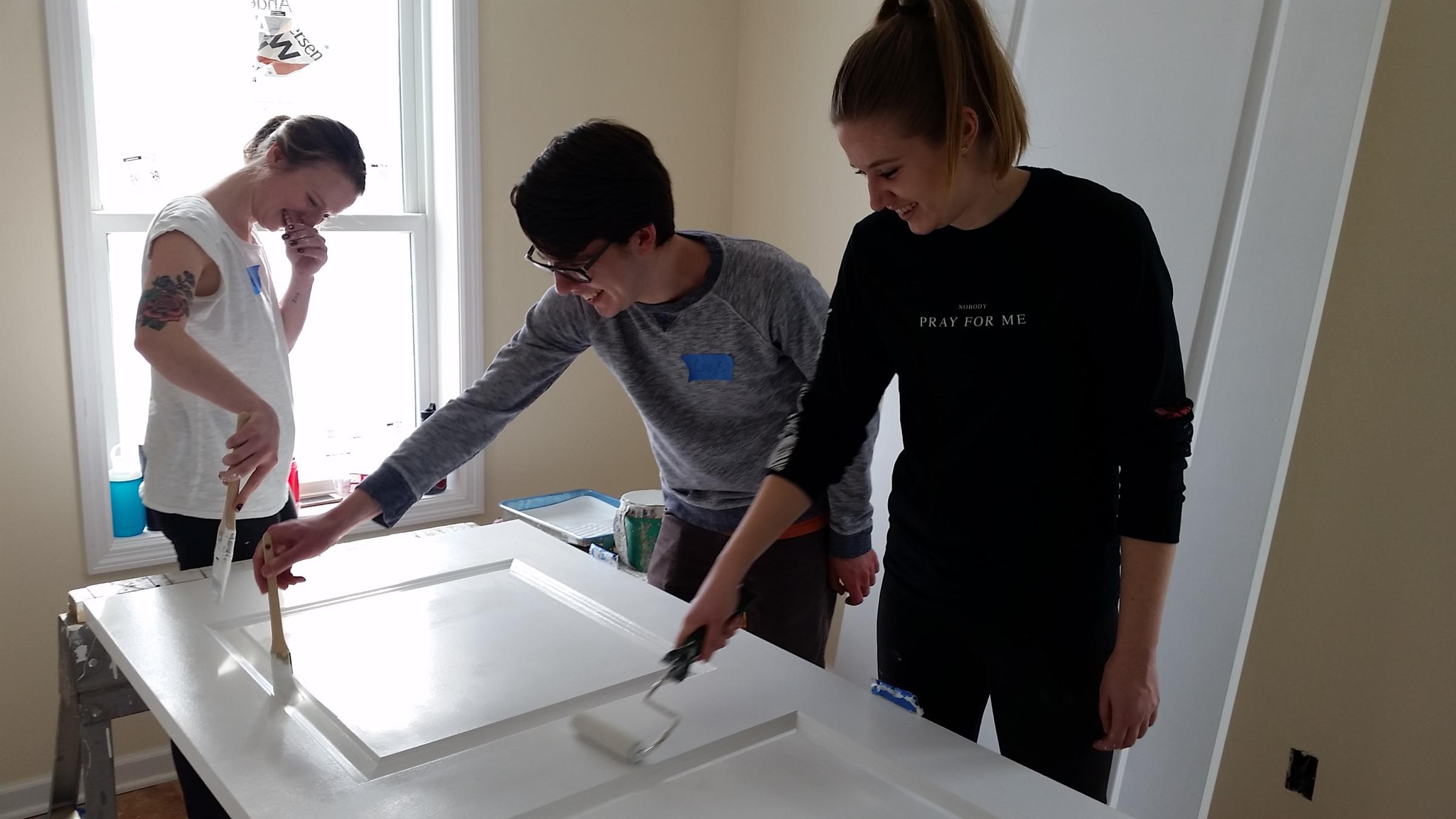 Three people painting a door