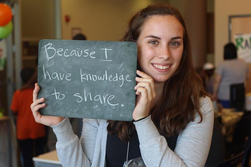 Woman holding a sign stating, "Because I have knowledge to share."