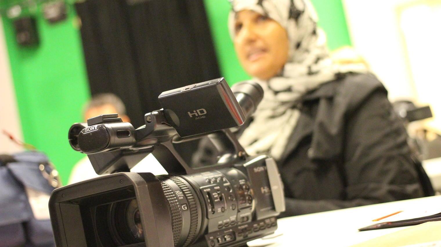 in the foreground their is a camera and blurred in the background is a woman in a hijab